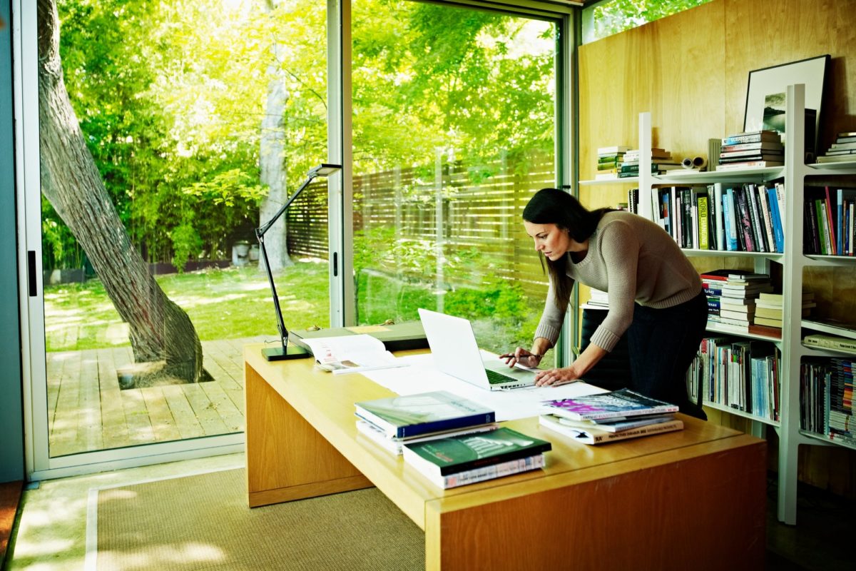 Woman standing at desk over laptop with view of backyard