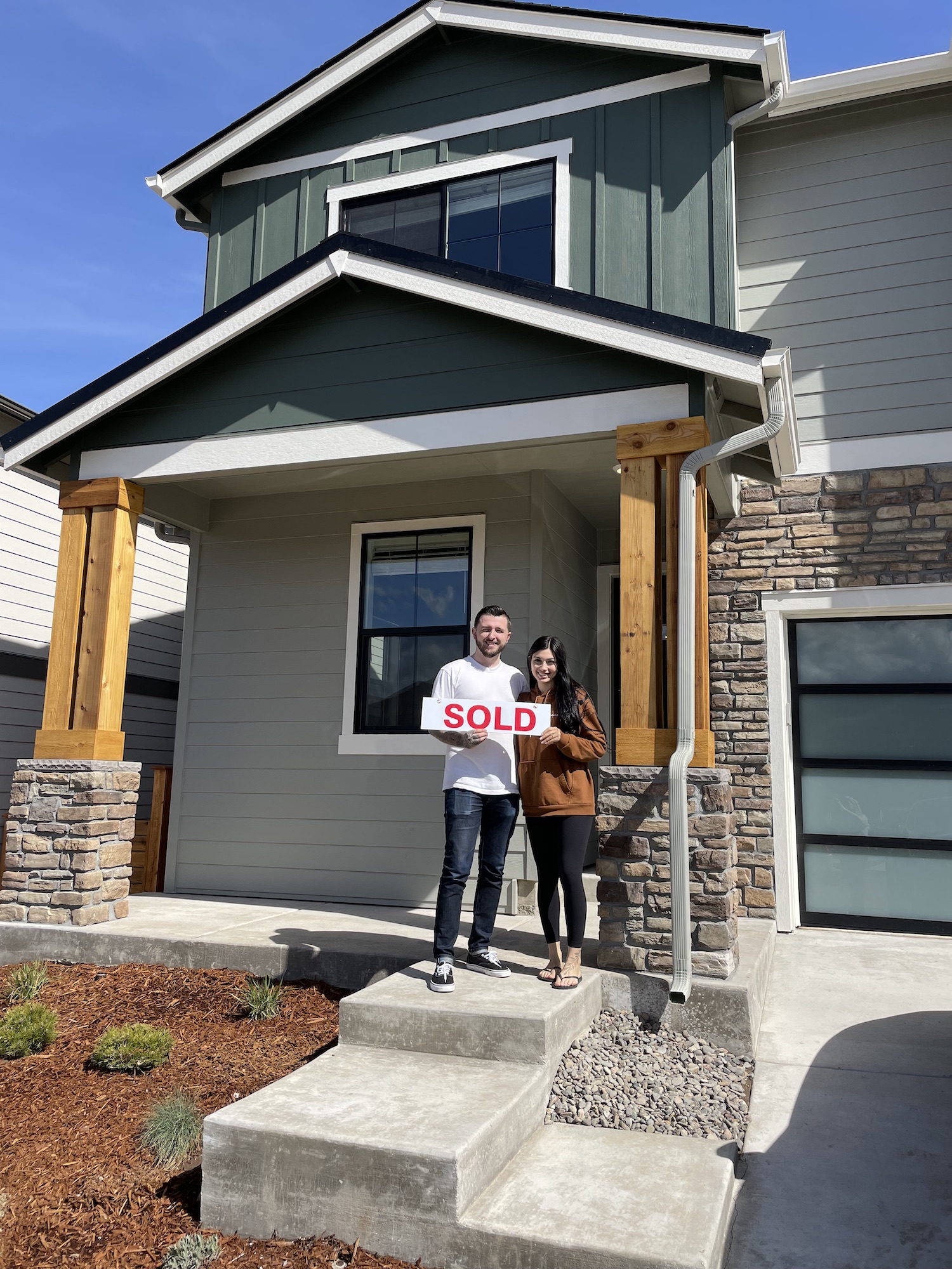 couple holding sold sign in front of green house