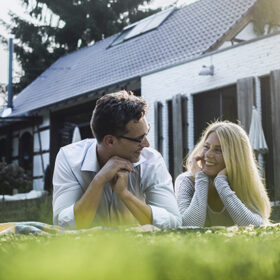 Happy mature couple lying on meadow in front of their house