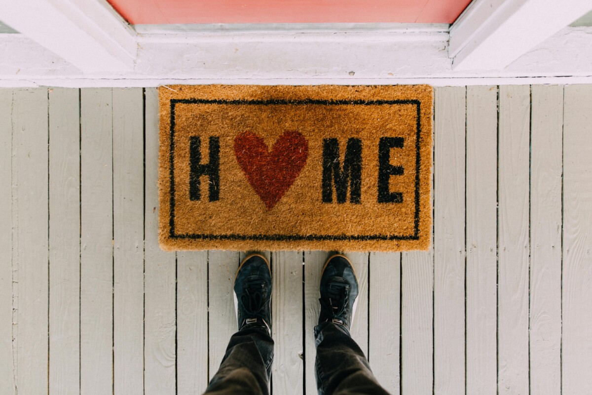looking down at two feet and a welcome mat with the word home spelled with a heart